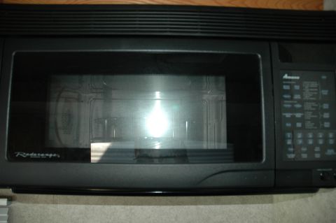 2005 Chevrolet C-6500/Kodiak - This is a black over-the-range microwave with a digital control panel and a glass door showing the interior.