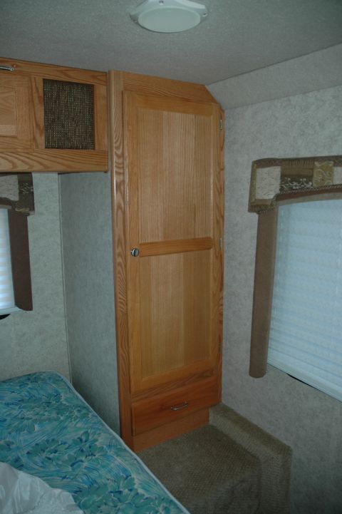 2005 Chevrolet C-6500/Kodiak - Interior view of an RV showing wooden cabinetry, a bed, and blinds on the window.