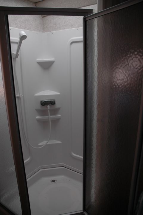 2005 Chevrolet C-6500/Kodiak - Interior view of a white RV shower stall with a showerhead and drain visible.