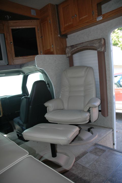 2005 Chevrolet C-6500/Kodiak - The interior of an RV shows a comfortable captain's chair with an ottoman, facing the driver's seat.