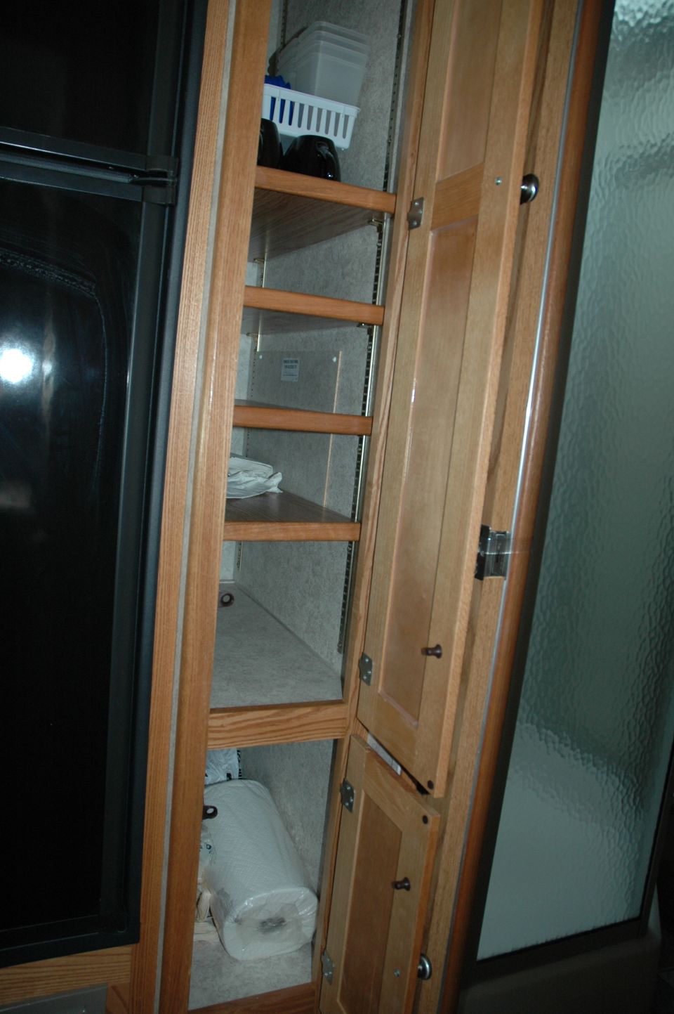 RV interior tall cabinet with shelves and doors, holding paper towels and a basket
