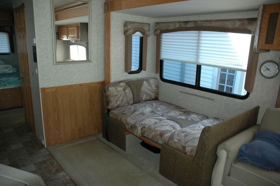 RV interior with a pull-out bed, wood paneling, and a mirror reflecting a cabinet