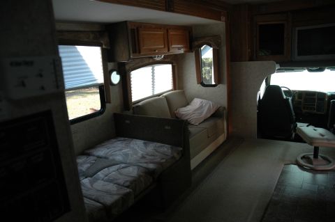 2005 Chevrolet C-6500/Kodiak - Interior view of an RV, a sleeping area and seating, with a glimpse of the driver's cockpit.