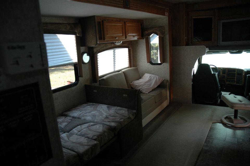 RV interior showing a fold-out bed, sofa, and the driver's cabin