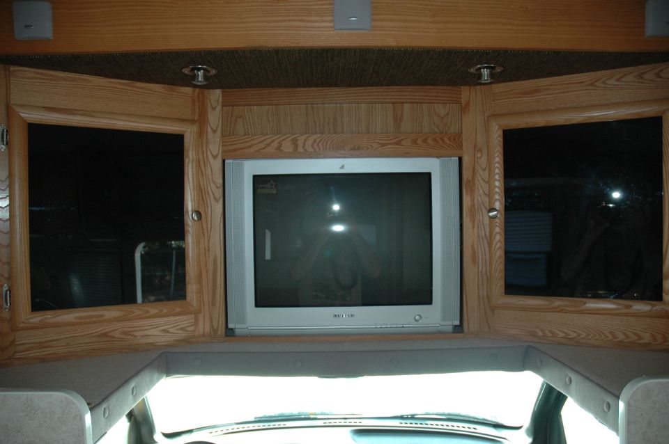 Tube TV mounted in oak cabinetry overhead inside an RV or motorhome