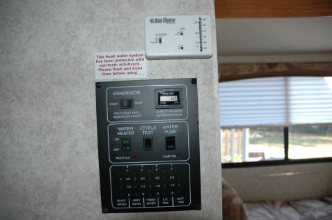 2005 Chevrolet C-6500/Kodiak - Control panel for generator, water heater, and tank levels, alongside a Duo-Therm thermostat, inside an RV.