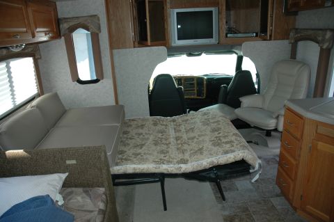 2005 Chevrolet C-6500/Kodiak - The interior of an RV shows a bed set up in the living area, with the driver's seats visible through an opening.