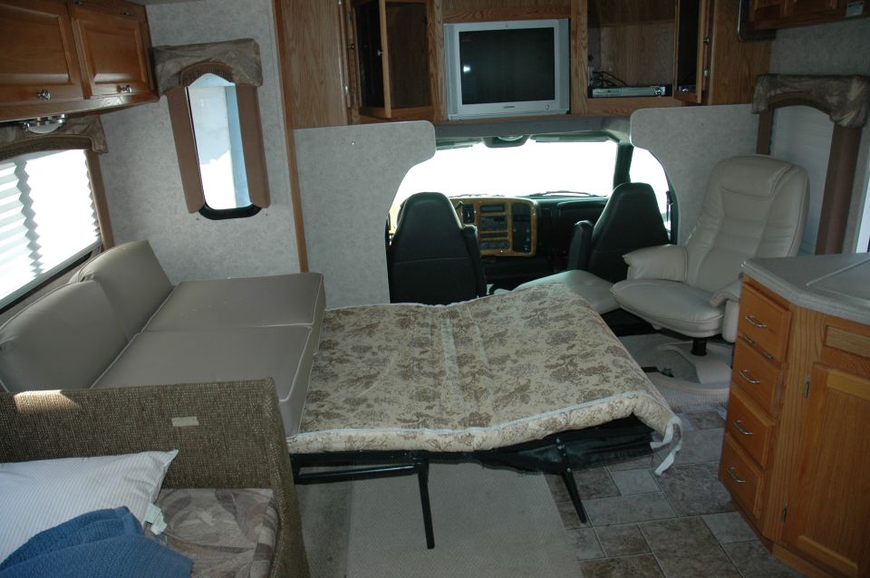 RV interior showing a fold-out bed, couch, and the driver's cabin