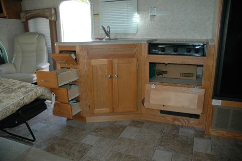 2005 Chevrolet C-6500/Kodiak - Interior view of an RV kitchen oak cabinetry, a sink, and a stovetop, with drawers and cabinets visible.