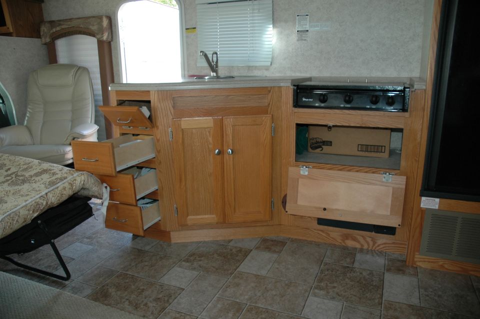 RV interior kitchen with oak cabinets, open drawers, sink, and stove