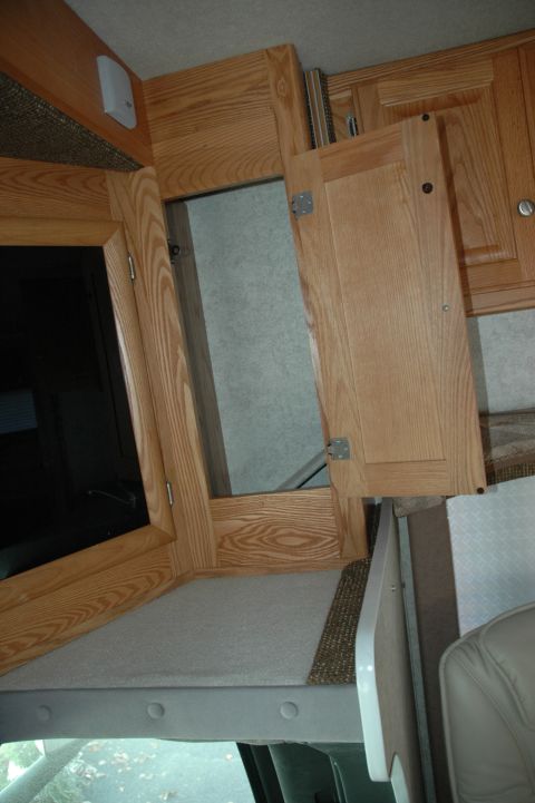 2005 Chevrolet C-6500/Kodiak - Close-up view of the wooden cabinets and mirrored door inside an RV's living space.