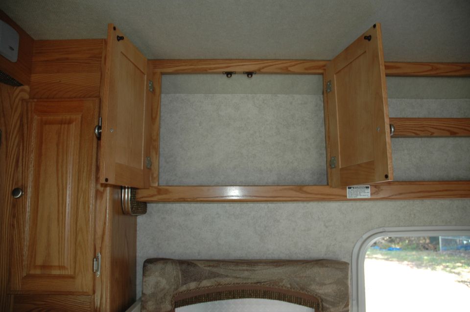 Interior view of RV cabinets, one door open, showing wood grain and textured walls