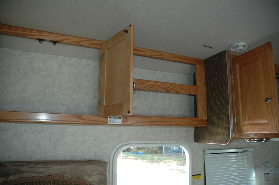 RV interior with open wooden cabinets and a window showing trees outside