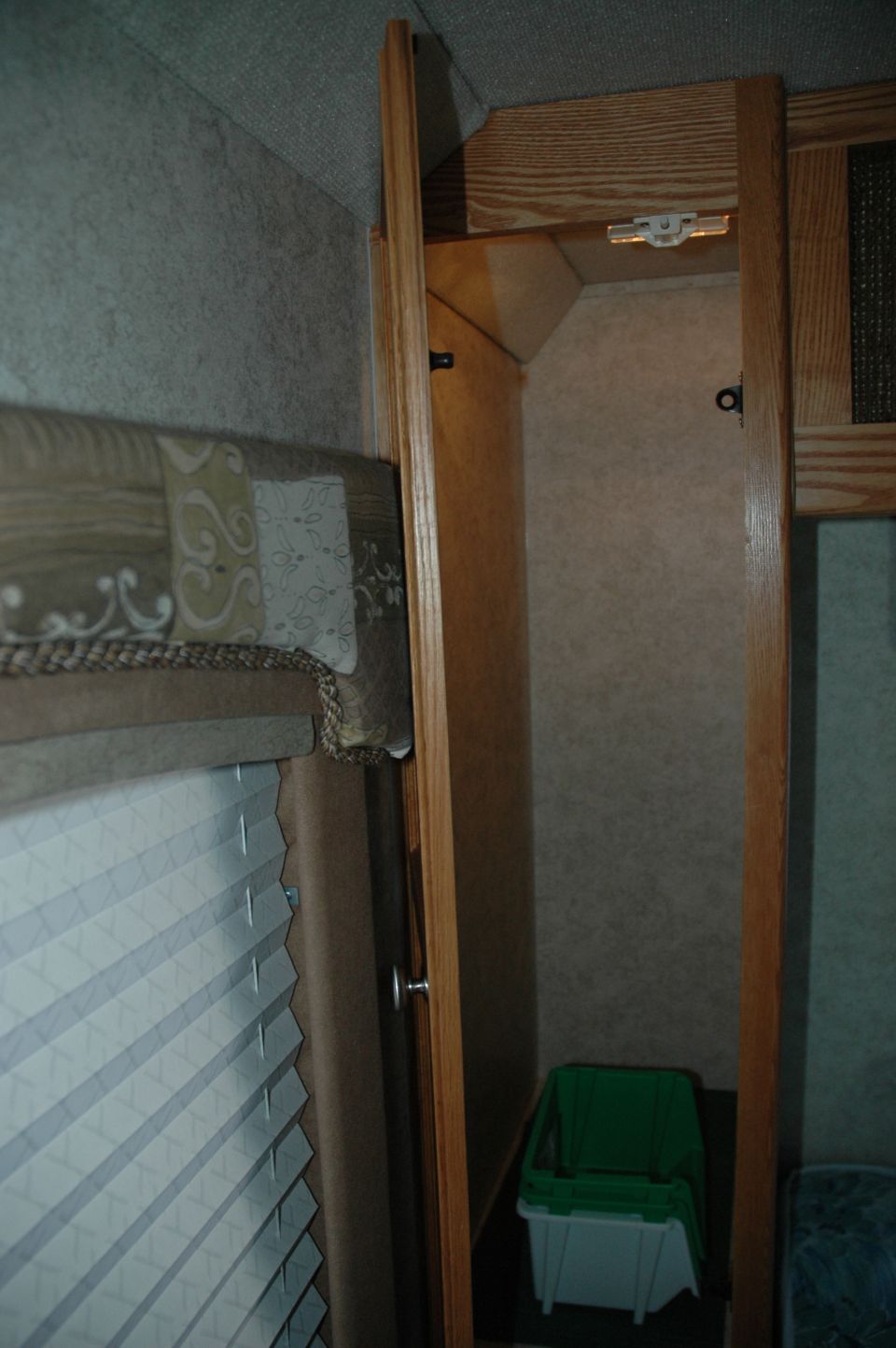 Interior corner of an RV or camper showing wood cabinet and pleated shade
