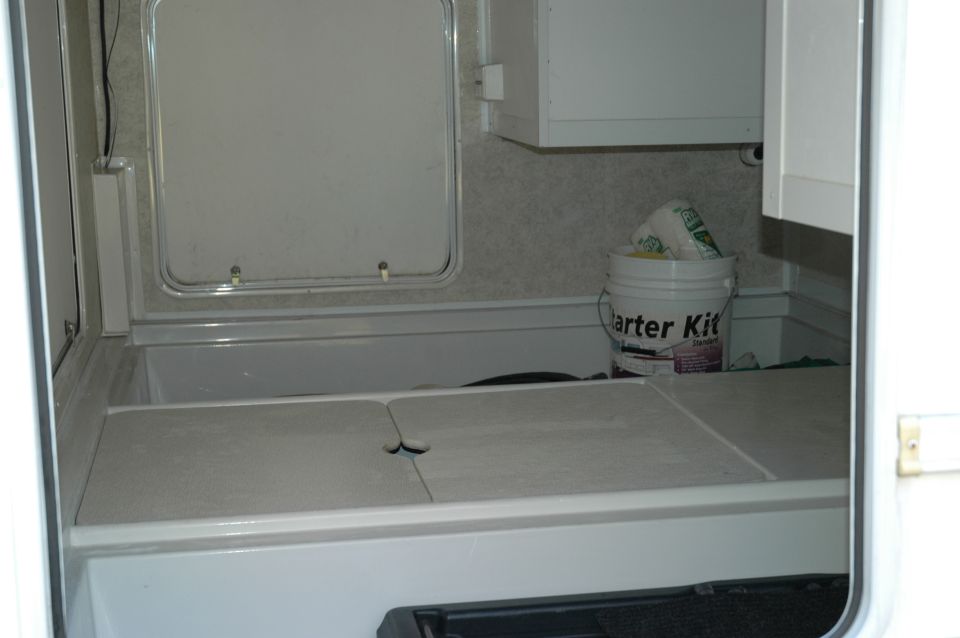 RV interior with a white bucket labeled "arter Kit" and a closed compartment