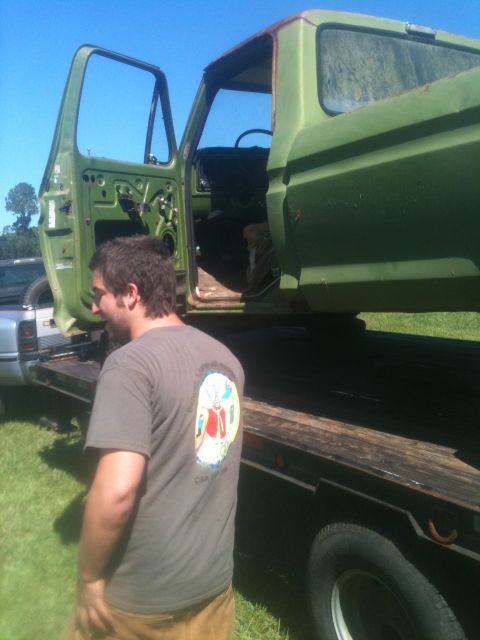 1993 Ford Bronco - A man stands next to a green pickup truck being transported on a flatbed trailer, with both the driver and passenger doors open.