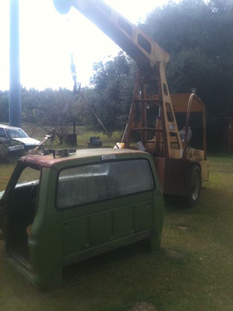 1993 Ford Bronco - A green truck cab sits in front of a yellow crane in a grassy outdoor area.