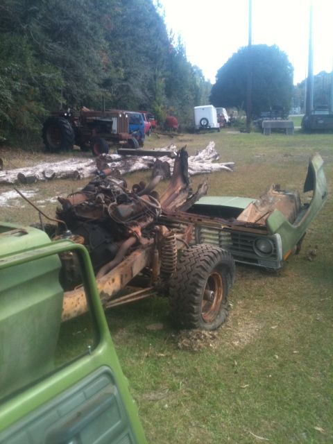 1993 Ford Bronco - This is a wrecked truck chassis with its engine exposed, sitting in a grassy yard with other vehicles.