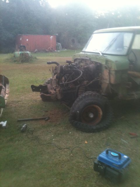 1993 Ford Bronco - Green truck with its front end dismantled, showing the exposed engine and a flat tire on a grassy area.