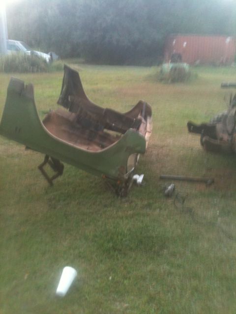 1993 Ford Bronco - A green vehicle tub is seen disassembled and lying on the grass in a yard, with other parts and a distant building in the background.