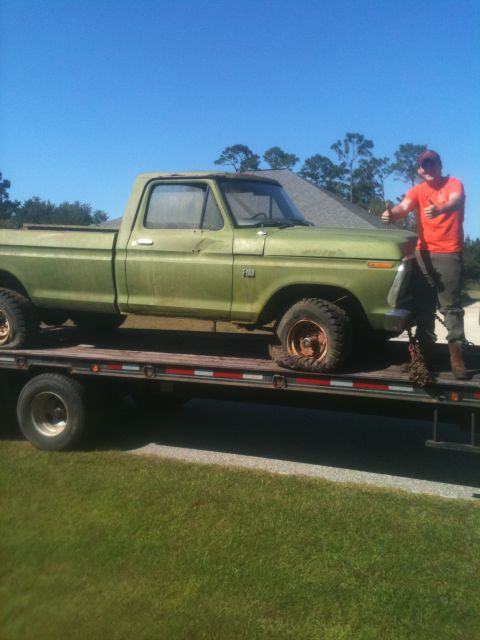 1993 Ford Bronco - A man stands next to a green Ford F-Series pickup truck being transported on a flatbed trailer.