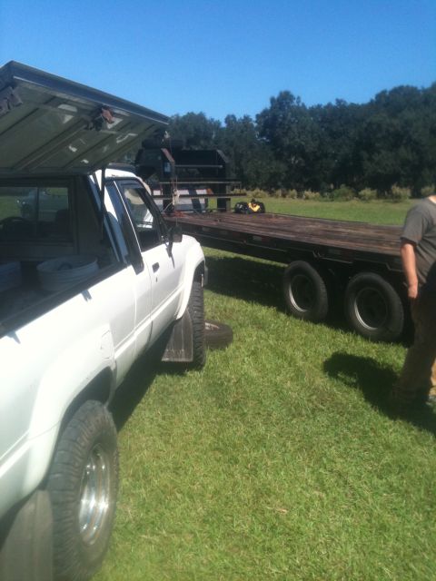 1993 Ford Bronco - A white pickup truck is parked on grass next to a large flatbed trailer under a clear blue sky.