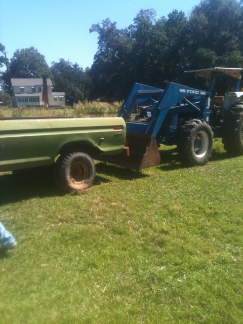1993 Ford Bronco - A green pickup truck is parked next to a blue Ford tractor with a front loader in a grassy field.