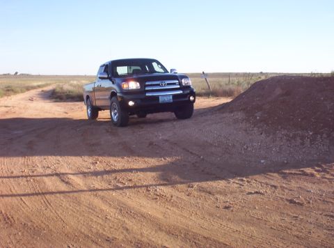 1988 Ford Bronco - A black Toyota Tundra is shown driving on a dirt road with a clear sky overhead.