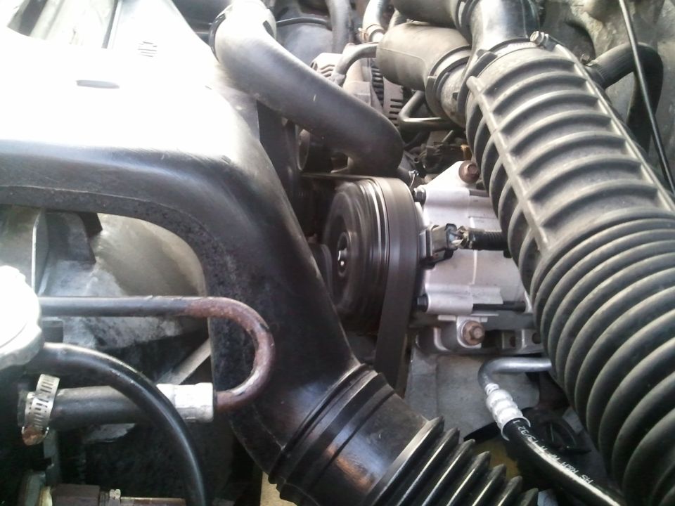 Engine bay view of AC compressor, belt, and hoses