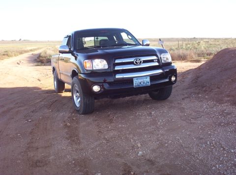1988 Ford Bronco - A black Toyota Tundra pickup truck drives on a dirt path in a dry, open landscape.
