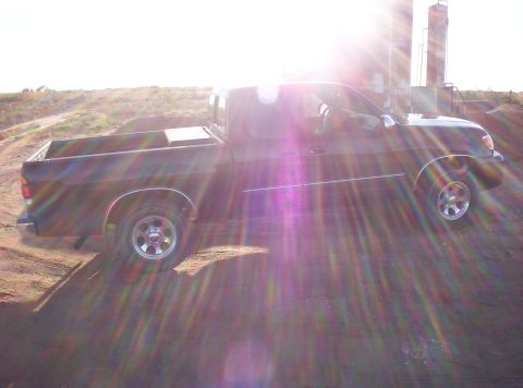 1988 Ford Bronco - Black pickup truck parked on a dirt road with sun flare.