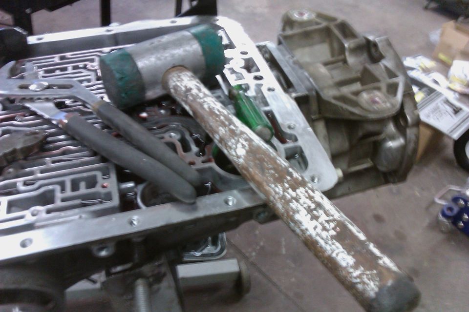 Transmission valve body with a rubber mallet and pliers on top. Another transmission component is visible to the right