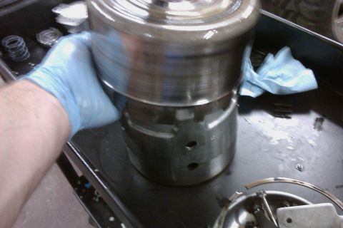 2005 GMC Yukon - A mechanic's gloved hand holds a metal part, possibly from a transmission, with a blue shop towel in the background.