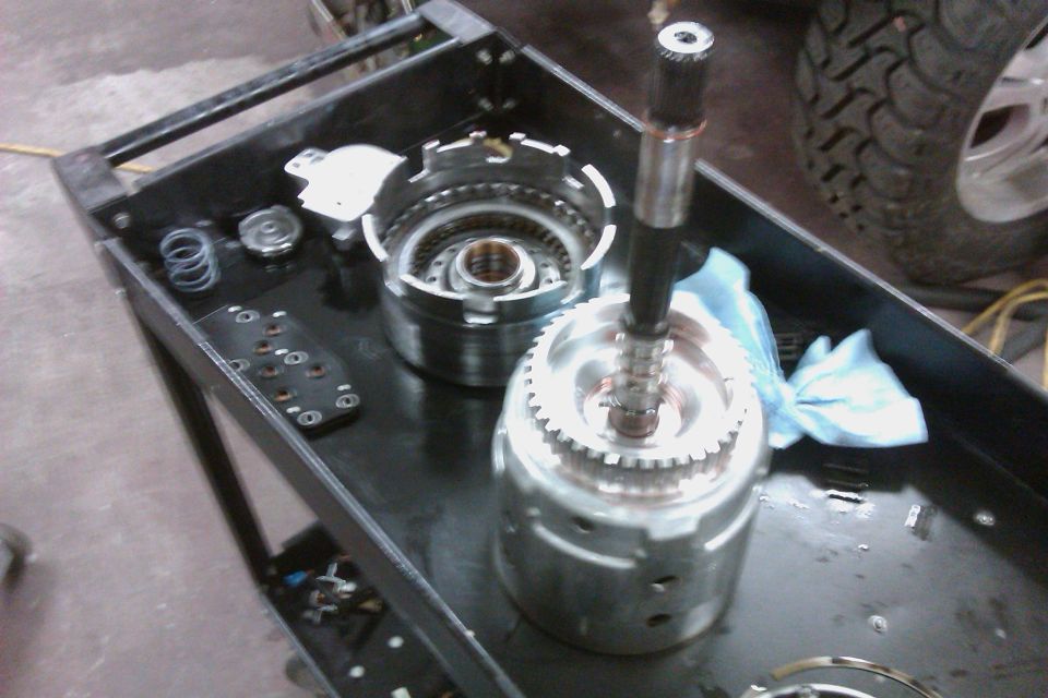 Transmission components disassembled on a black cart, with a tire visible in the background