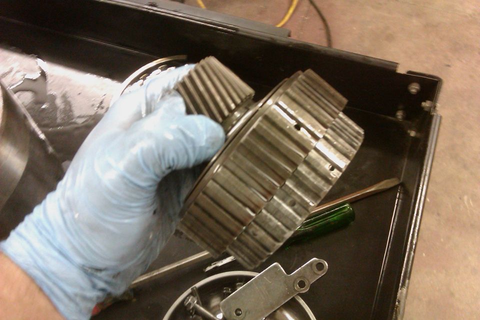 Gloved hand holding transmission gears. Tools and parts in a toolbox