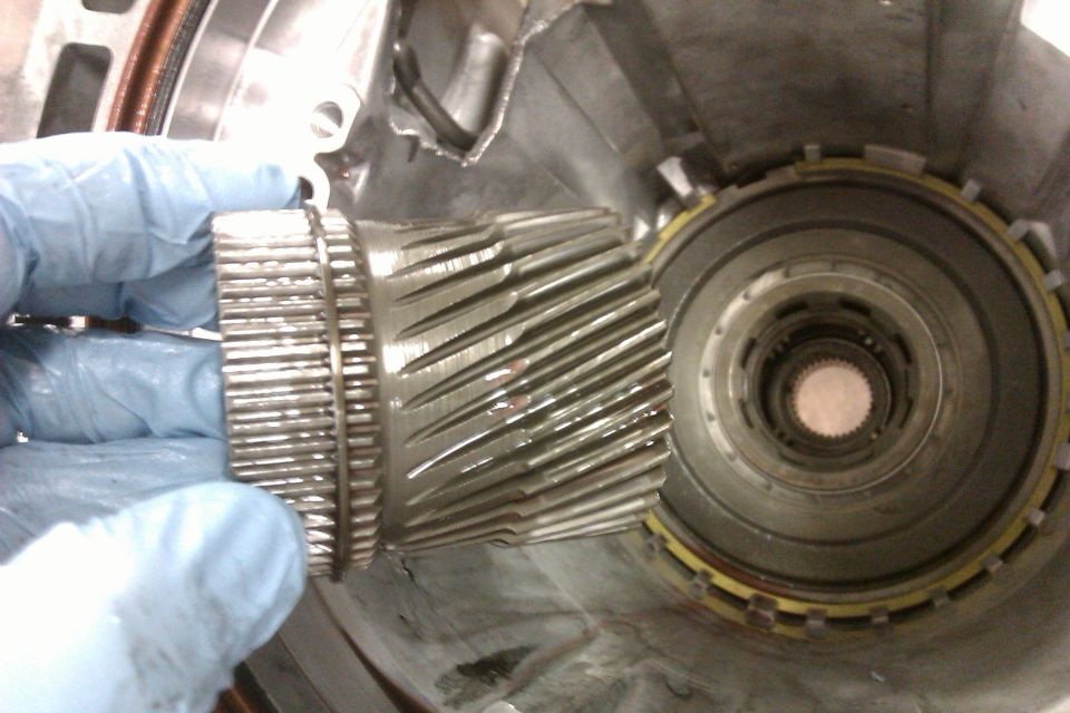 Gloved hands holding a transmission gear set inside a transmission housing