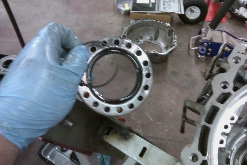 Gloved hand holding a transmission seal ring with a metal housing in the background