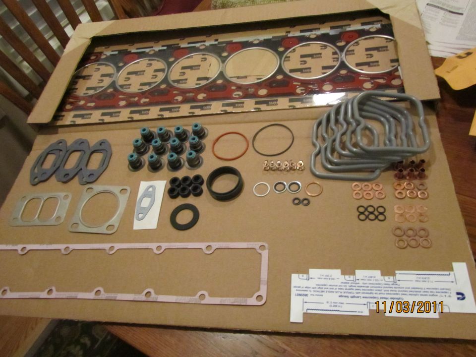Engine gasket set laid out on cardboard. Includes head gasket, valve seals, and various other engine seals and gaskets