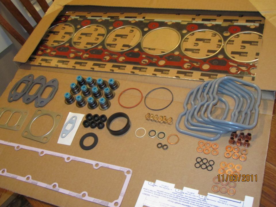 Engine gasket set with head gasket, valves, and seals laid out on cardboard
