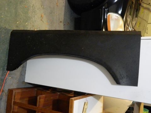 1979 Ford Bronco - A black fender part is shown resting on a white surface, with a vehicle's headlight visible in the background.