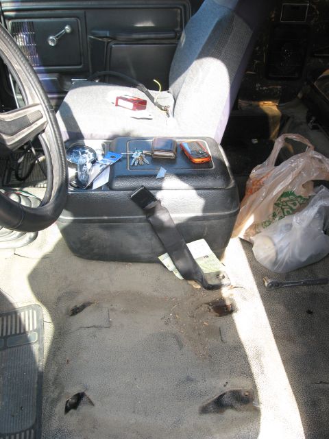 1981 Ford Bronco - The interior of a vehicle shows wear and tear on the floor, with a center console holding various items.