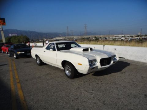 1972 Ford Ranchero - A white 1972 Ford Ranchero with a prominent hood scoop is seen from the front-right angle, with other vehicles lined up behind it.