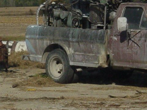 1992 Ford Bronco - This weathered pickup truck appears to be carrying a load of machinery in its bed.