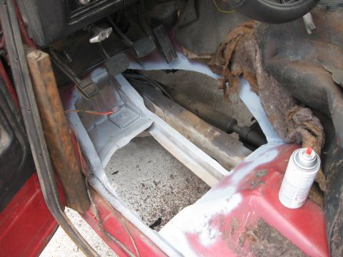 1981 Ford Bronco - The interior floor of a red vehicle is undergoing rust repair, with primer and exposed metal visible.