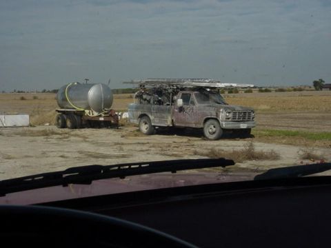 1992 Ford Bronco - A weathered pickup truck tows a large water tank trailer across a dry, rural landscape.