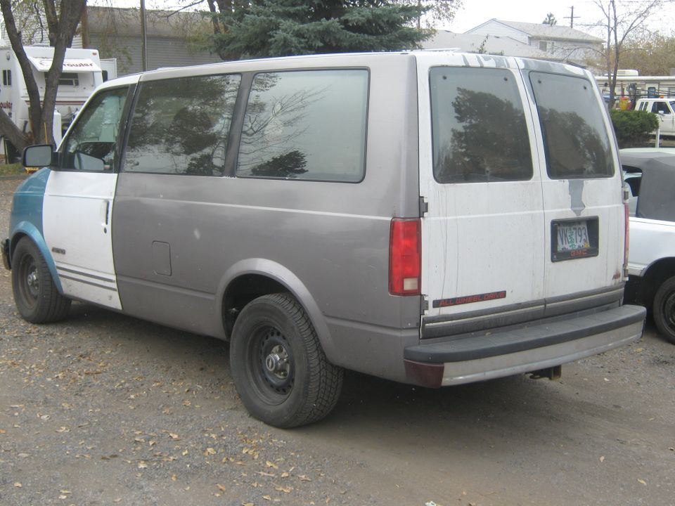 Gray and white GM Safari van with all-wheel-drive badge, rear three-quarter view