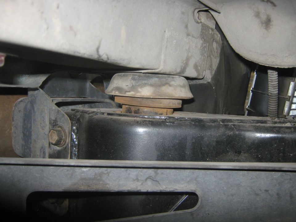 Undercarriage view of a vehicle's suspension mount with rubber isolator and metal brackets