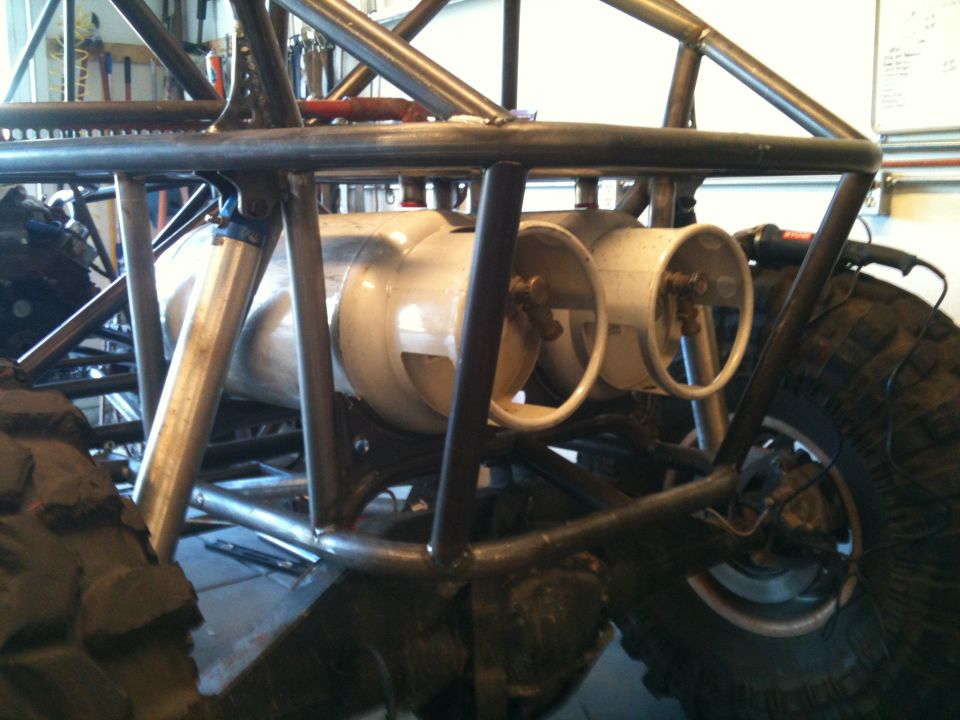 Off-road buggy frame with two large fuel tanks visible, rear tire and suspension components also shown