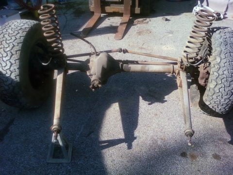 1989 Ford Bronco - Front axle and suspension parts are laid out on the ground, with a forklift visible in the background.