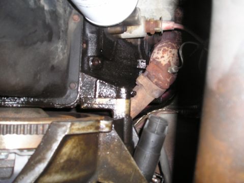1997 Ford F-250 - Close-up view of an engine's oil pan and exhaust manifold, showing signs of oil leakage and rust.